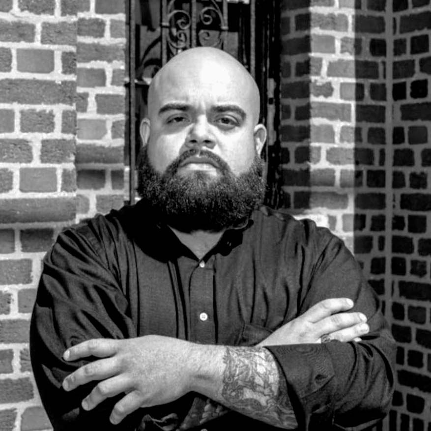 Black and white photograph of Father Michael Lopez with a brick building in the background