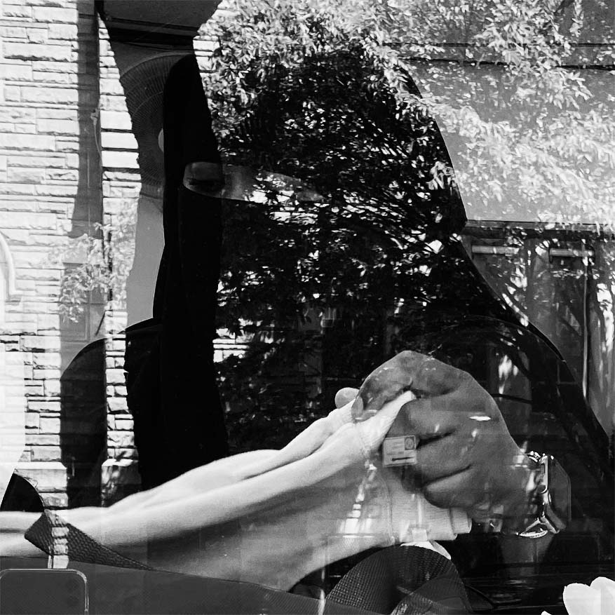 Black and white photograph of a person seen through a window with reflection of a tree and building from the opposite direction