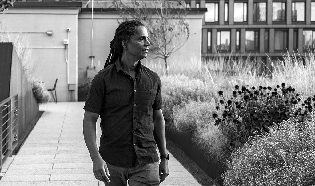 Black and white image of Mark Winston Griffith walking on a Brooklyn rooftop